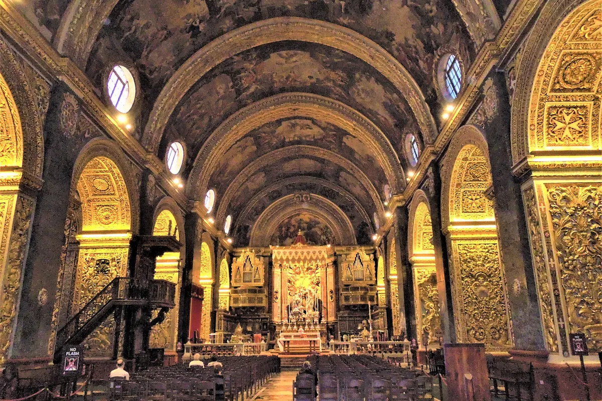The nave of St John's Co-Cathedral looking towards the altar, with a painted barrel vault above and walls covered in gilded carving