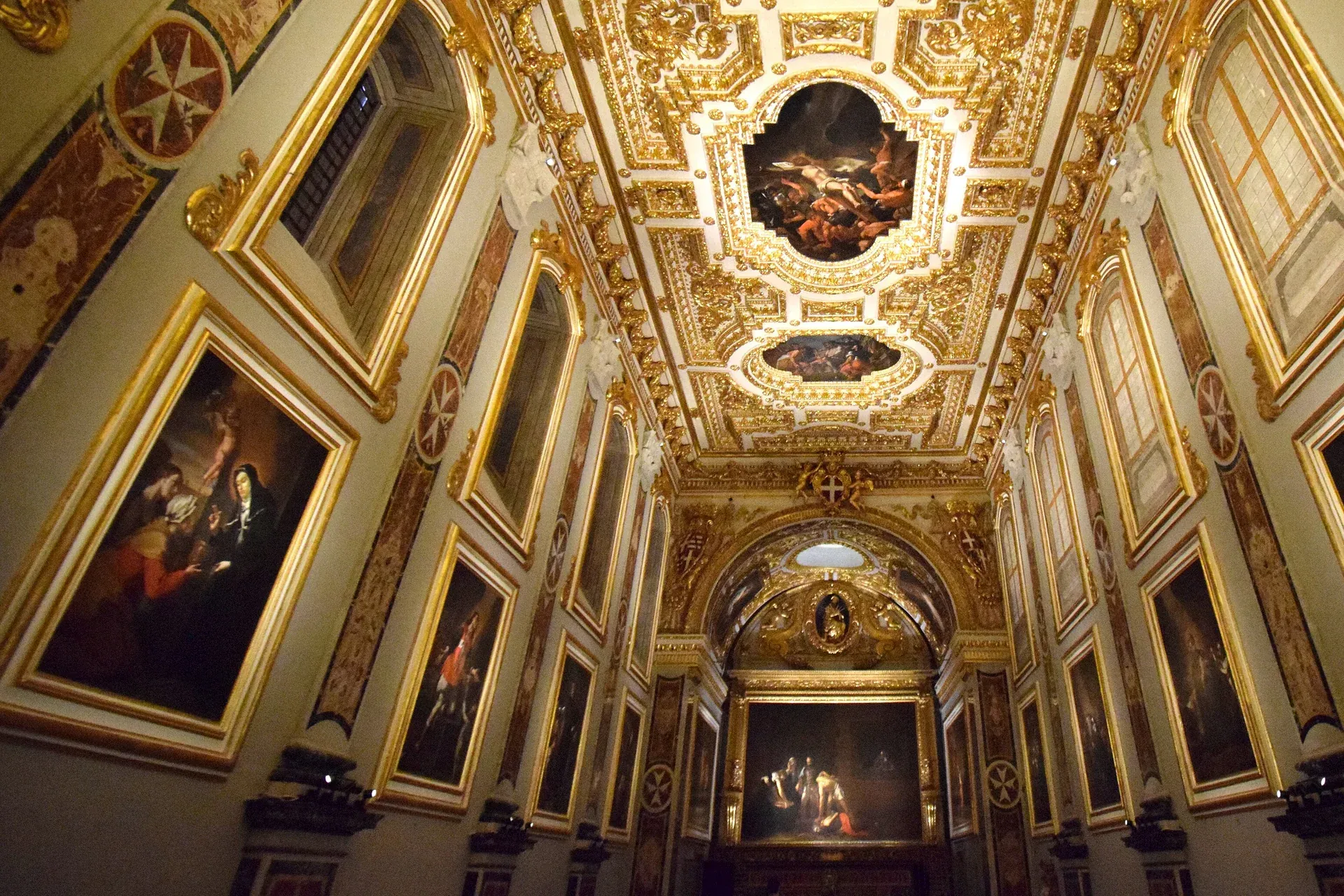 The Oratory of St John's Co-Cathedral in Valletta: a long gilded hall hung with large dark paintings, a carved and gilded ceiling above, and Caravaggio's Beheading of Saint John the Baptist glowing at the far end